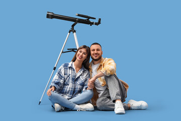 Young couple with telescope sitting on blue background