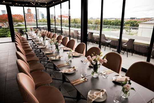 Elegant rooftop event table setup with modern dining d&eacute;cor, floral centerpieces, and panoramic Vilnius city views, arranged for a stylish celebration, wedding reception, or upscale gathering.