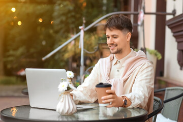 Young male programmer with coffee and laptop working at table in street cafe