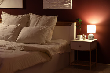 Glowing lamp with plant on nightstand in dark bedroom