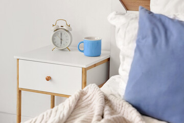 Alarm clock with cup on bedside table in light room
