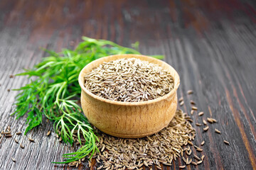 Cumin seeds in bowl with herbs on dark board