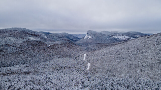Aerial view of a snow-covered road crossing the snow-covered boreal forest and heading towards the mountains on a winter day.