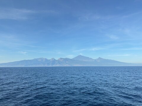 Vast blue ocean meets distant majestic mountain range under clear sky, evoking serenity and adventure for travel and nature lovers