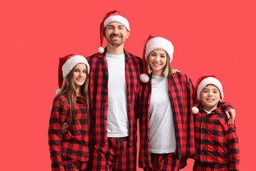 Fototapeta premium Happy family in pajamas with Santa hats hugging on red background
