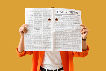 Young woman looking through holes cut in newspaper on yellow background. Search concept