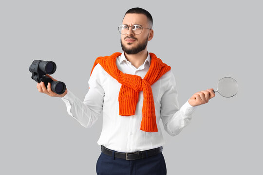 Thoughtful businessman with binoculars and magnifier on light background. Search concept