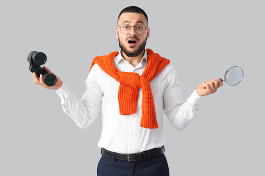 Shocked businessman with binoculars and magnifier on light background. Search concept