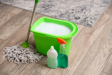 Mop with green bucket and detergents on floor in living room