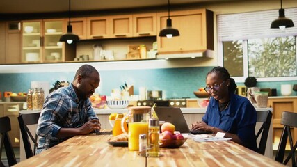 African American partners organizing financial paperwork and tax receipts at home. Checking numbers for home finances and accounting on a laptop, reflecting responsible financial habits. Camera A.