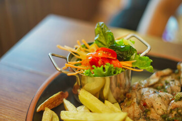 Small metal container with some salad inside: carrot, tomato, and lettuce.