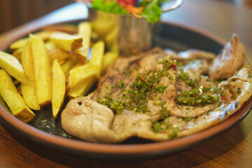 Pork steak with parsley on top, served with fries and a bowl of salad.