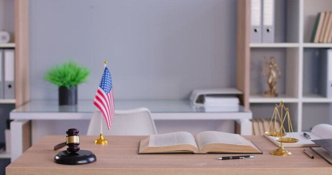 Interior of modern office of judge or lawyer with scales, wooden gavel and american flag on table. Empty courtroom with nobody at workplace. Justice and legal law concept. 4k video.