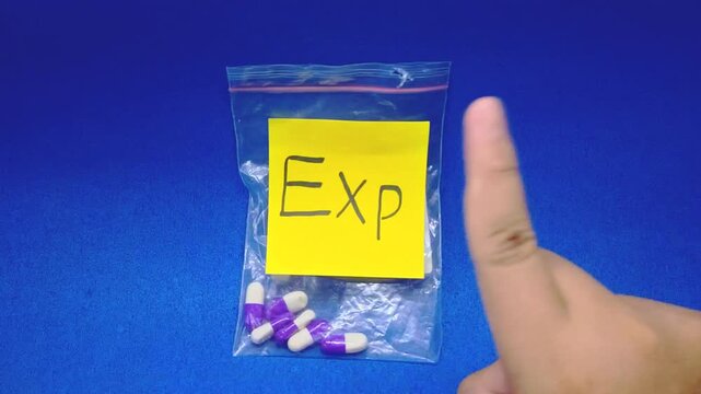 Expired medicine in a plastic bag, a hand points at the label 'Exp' on a yellow sticky note, close-up shot