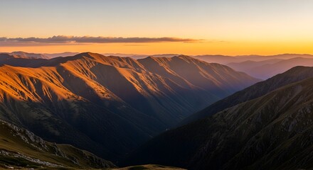 Golden light of dawn beautifully illuminates the majestic rugged mountain peaks and deep valleys, creating dramatic long shadows across the ancient, sprawling landscape during sunrise