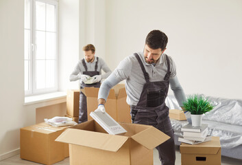 Team of young confident professional workers movers of moving service in overalls delivering and...