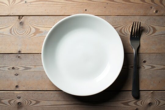 A simple, elegant place setting featuring a pristine white dinner plate and a sleek, metallic fork on a rustic wooden table - Powered by Adobe
