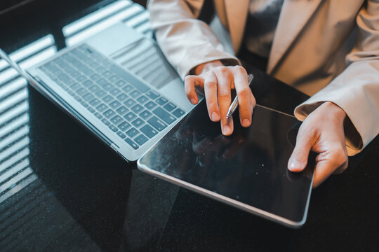 Businessperson using a tablet and laptop in a modern office, showcasing digital technology in professional work. - Powered by Adobe