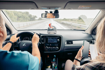 driver holding steering wheel in modern car while passenger sits in front seat, road trip, interior dashboard, navigation screen, rearview mirror reflection, travel, transport