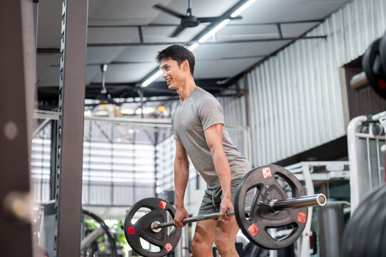 Happy asian man client in sportswear standing holding barbell exercising doing weight lifting in gym - Powered by Adobe
