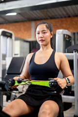 Fototapeta premium Asian woman fitness trainer or client sitting while exercising with stretch equipment machine in gym