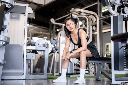 Asian woman client or fitness trainer coach sitting sitting on bench resting after exercising in gym