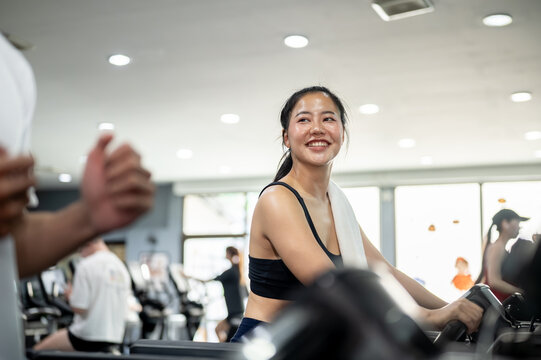 Pretty asian woman client or fitness trainer coach talking as exercising running on treadmill in gym