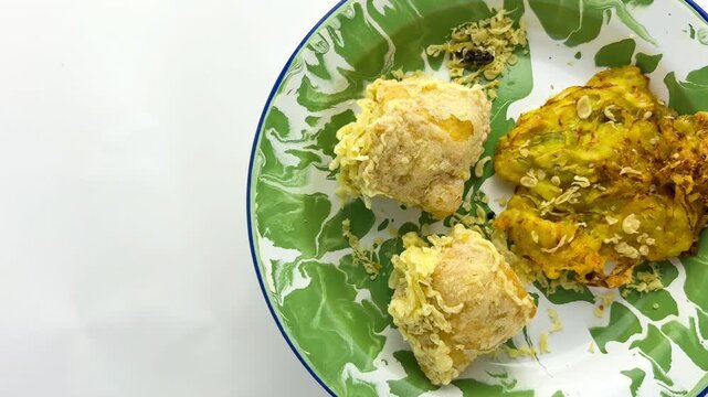 Indonesian fried bakwan and tofu on a green enamel plate, highlighting unhealthy eating habits due to oily, high-calorie fried snacks often found in local street food. flat lay