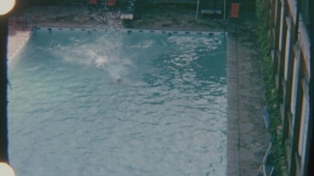 Adult Male Leaps From Diving Board Into Pool Water