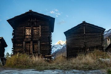 Snow Capped Mountains Hide Behind Two Traditonal Buildings In The Swiss Alps