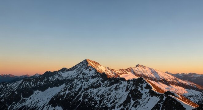 Snow-capped mountains at sunset with a clear blue sky.