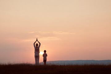 young man stands by window with cup of coffee in his hands smiling as sunlight filters in