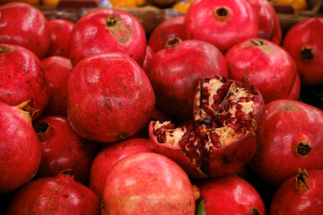 Market stall with whole pomegranates and one split open to reveal glistening red seeds