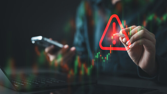 A person analyzing a trading chart with a glowing warning symbol, representing market volatility, investment risk, financial decline, and strategic decision-making during crisis situations.