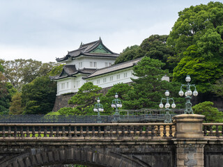 Obraz premium The historic Stone Bridge spans the moat leading to the Imperial Palace grounds in Tokyo, framed by lush green trees and traditional Japanese architecture.