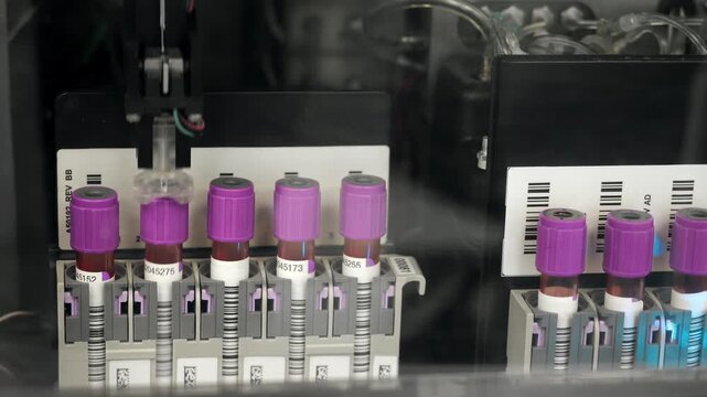 Closeup of blood tubes with EDTA caps moving inside automated hematology analyzer in clinical lab setting indoors.