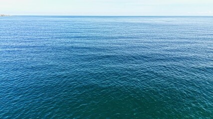 Gentle waves glide across the tranquil ocean surface under a bright sky. The clear water reflects the sunlight, inviting a sense of peace and relaxation by the shore.