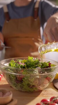 Woman in apron pouring olive oil from cruet on fresh green salad vertical slow motion closeup Mediterranean diet healthy fats home cooking lifestyle organic food