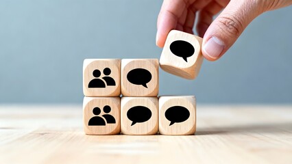 Communication and Collaboration Concept Hand Placing Wooden Block with Speech Bubble Icon atop Blocks with People Icons, on Wood Table, Pale Blue Background