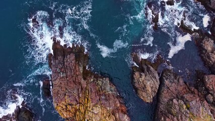Waves crash against the rocky shore in this breathtaking coastal scene. The vibrant blue water contrasts with the textured rocks, creating a stunning view of nature's power and beauty.