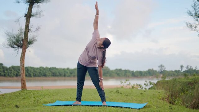 Female performing triangle pose in a calm natural setting in early morning, promoting wellness, calm energy, and stress relief.