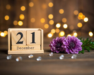 Wooden Calendar Showing December 21st with Purple Flowers and Lights Bokeh Close up Photo