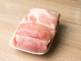 Fresh raw pork meat on white tray on wooden kitchen table