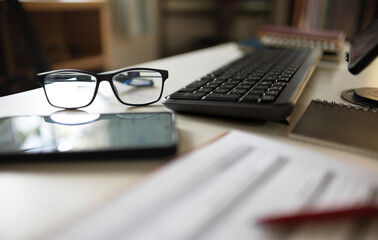 close up shot, eyeglasses with mobile phone, computer keybord, notebook and document on desk office