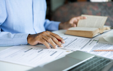 Fototapeta premium asian man checking business document find knowledge in book using laptop to working online via internet technology, close up shot