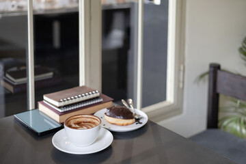 coffee cup with latte coffee and mobile phone, book for read, diary for taking note and donut on black table