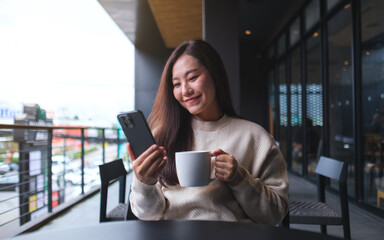 Portrait image of a woman holding and using mobile phone while drinking coffee in cafe
