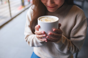 Closeup image of a woman holding a cup of hot caramel macchiato coffee