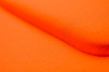 Close up of vibrant orange textile or synthetic fabric texture with small pores, folds, and deep shadow detail. Concepts of fashion material, bright color background, abstract pattern.