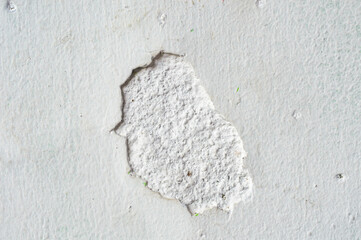 Close up of a damaged white plaster wall showing a chipped section of rough interior concrete texture. Concepts of renovation, decay, grunge background, construction, crack, and destruction surface.